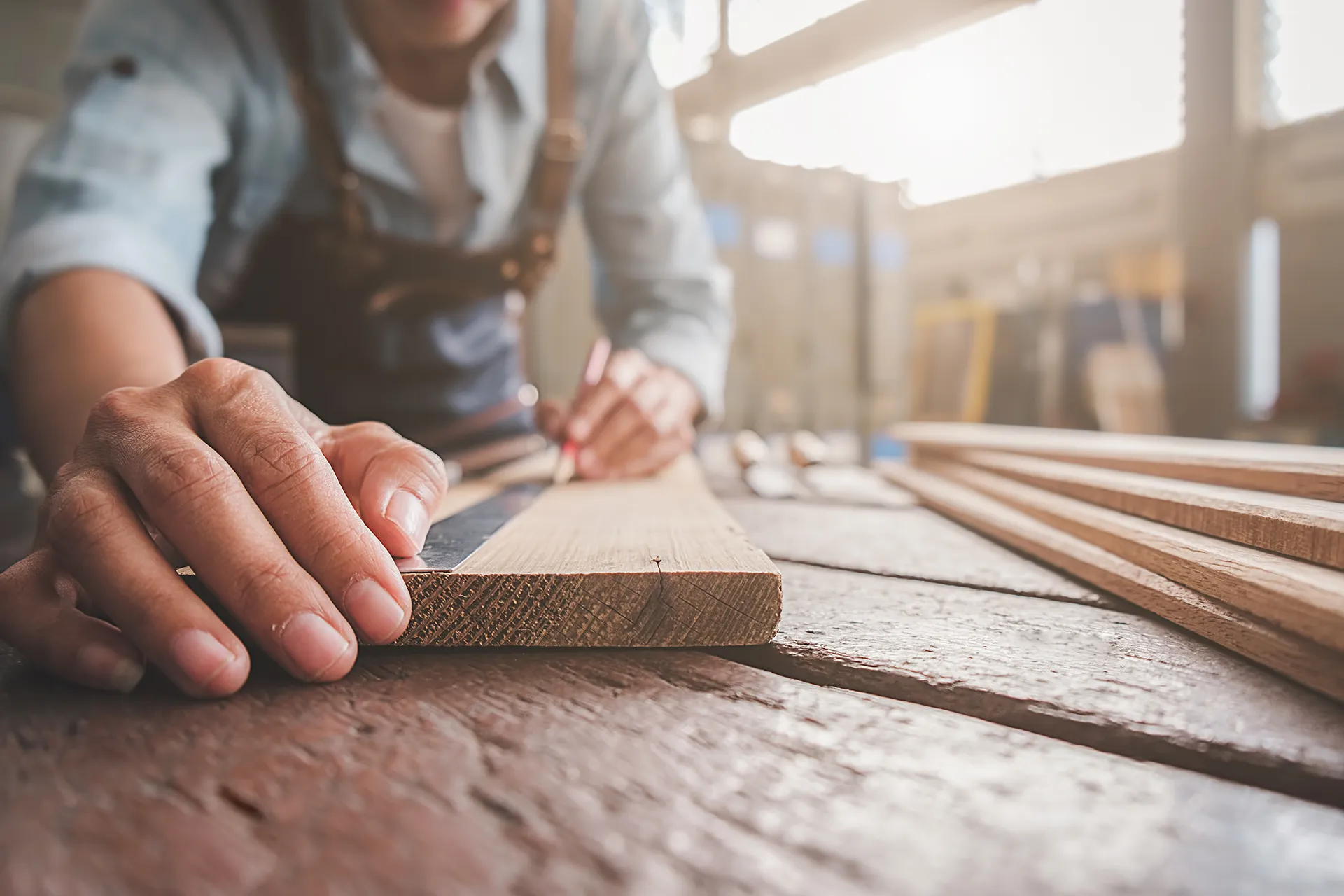Close-up of a carpenter using a ruler and pencil to mark measurements on a wooden plank in a sunlit workshop