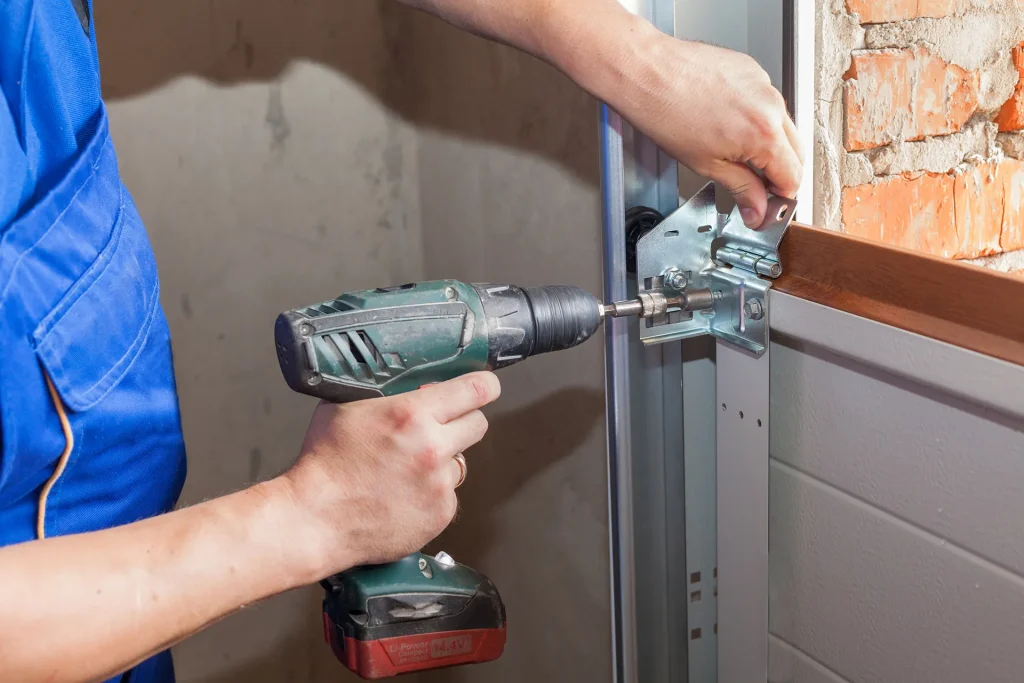 $\text{Worker installing a new sectional garage door hinge using an electric drill}$