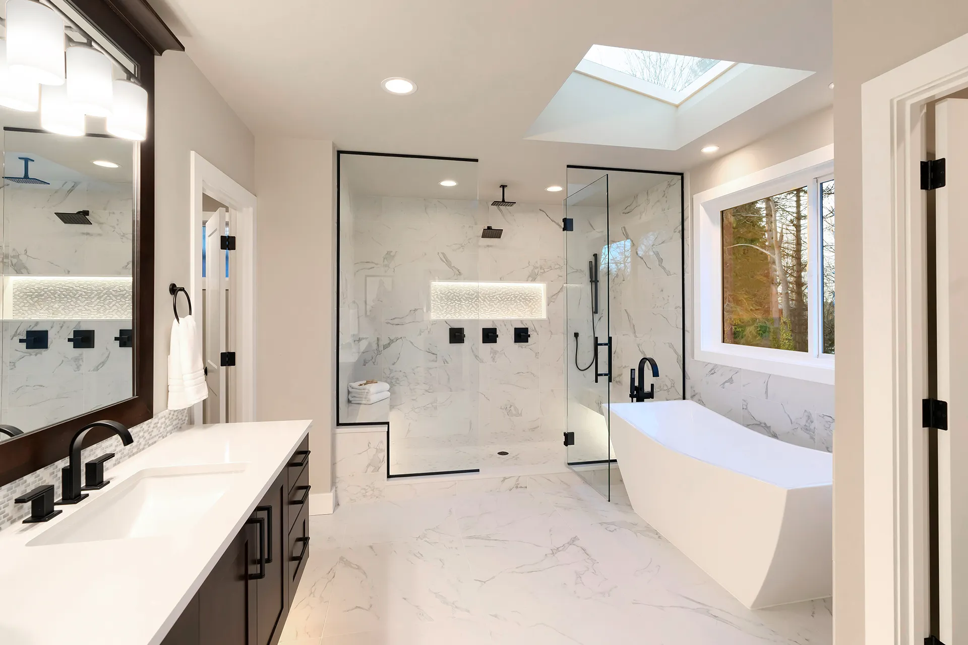Luxury modern master bathroom with marble-look tile, frameless glass shower, freestanding tub, and black fixtures