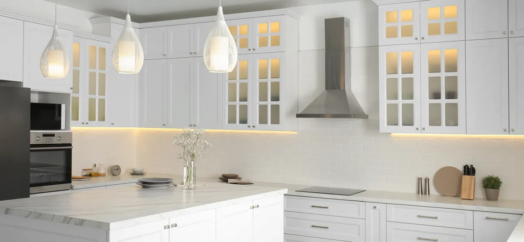 Modern white kitchen with glass front cabinets, under-cabinet lighting, large marble island, and unique woven pendant lights